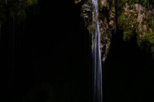Photographie minimaliste d’une cascade fine tombant sur fond sombre, illustrant la simplicité et l’impact visuel d’une composition épurée.