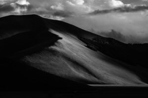 Photographie en noir et blanc d’une colline éclairée par une lumière rasante, mettant en valeur les textures et les contrastes.