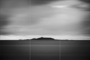 Photo minimaliste en noir et blanc montrant une île lointaine alignée selon la règle des tiers.