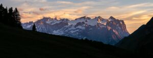 Panorama alpin assemblé au téléobjectif, montrant une chaîne de montagnes enneigées au coucher du soleil avec lumière dorée sur les reliefs.