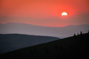 Coucher de soleil sur des collines superposées, photographié au téléobjectif avec compression des plans et silhouettes d’arbres en contre-jour.