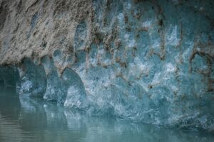 Texture bleutée et détails du front d’un glacier, photographiés au téléobjectif avec reflet dans l’eau – mise en valeur des motifs naturels.