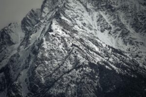 Flanc rocheux et enneigé d’une montagne cadré au téléobjectif, remplissant tout le champ de l’image pour révéler textures et contrastes minéraux.