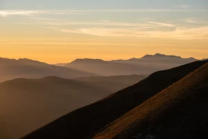 Coucher de soleil sur des montagnes successives éclairées par une lumière rasante et dorée.