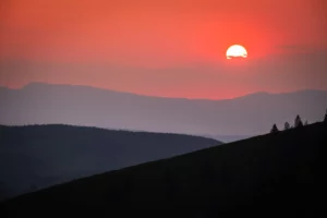 Coucher de soleil rouge intense projetant des silhouettes de montagnes dans une lumière chaleureuse.