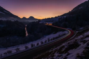 Traînées lumineuses de voitures réalisées en pose longue dans un paysage alpin au crépuscule.