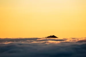 Sommet émergeant d’une mer de nuages au coucher du soleil, éclairé par une lumière dorée.