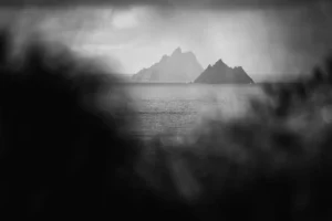 Avant-plan flou et sombre, mer et îles rocheuses au loin, photo de paysage en noir et blanc.