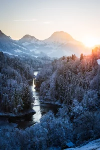 Vallée de montagne enneigée, rivière et forêt givrée au coucher du soleil